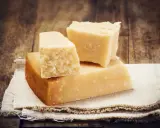 Drei Stücke Hartkäse, vielleicht Pecorino oder Parmesan, liegen auf einem Leinentuch vor rustikalem Holz.