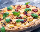Pizza mit Sahne statt Tomatensauce, belegt mit Kartoffeln, getrockneten Tomaten und frischem Basilikum.