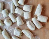 Vorbereitung für ein Grissini Rezept: Viele kleine, unregelmäßig geformte Teiglinge mit Kräutern liegen auf einem Holzbrett, bestäubt mit Mehl.