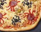 Gruselige Halloween-Pizza mit Spinnen aus Oliven und Salami, die über geschmolzenen Käse krabbeln.