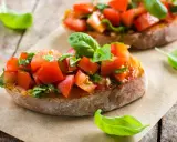 Zwei Bruschetta mit frischen Tomaten und Basilikum, warm oder kalt serviert, auf rustikalem Holztisch.