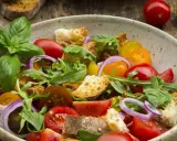Bunter Tomatensalat mit Brotstücken, Zwiebeln und Basilikum, verfeinert mit einem Hauch Balsamico Dressing.