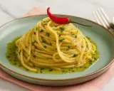 Ein Berg aus Spaghetti aglio e olio, garniert mit einer roten Chilischote und frischer Petersilie, auf einem mintgrünen Teller.