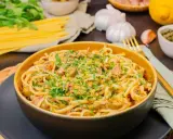 Eine Schüssel mit köstlicher Thunfisch Pasta, garniert mit Petersilie und Zitronenschale. Daneben liegen Spaghetti, Knoblauch und Kapern.