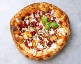 Pizza mit karamellisierten Zwiebeln, Speck, Pekannüssen und einem Hauch von Parmesan. Ein grünes Basilikumblatt krönt das Kunstwerk.