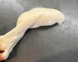 Ein Stück heller, klebriger Pizzateig wird von einer Hand gehalten und dehnt sich auf einer dunklen Arbeitsfläche aus.
