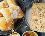 Frisch gebackene Ciabatta-Brötchen, bestäubt mit Mehl, liegen in einem Korb. Daneben zwei aufgeschnittene Scheiben mit luftiger Krume – perfekt zum ciabatta selber backen.