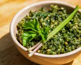 Schüssel mit würzigem Giersch Pesto, garniert mit frischen Kräutern auf Holzhintergrund.
