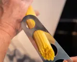 Ein Mann misst mit einem Metallwerkzeug die richtige Menge Spaghetti pro Person ab.