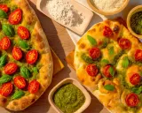 Zwei knusprige Pizzen mit leuchtend grünem Pesto, Kirschtomaten und frischem Basilikum. Daneben Schüsseln mit Pesto und Parmesan.