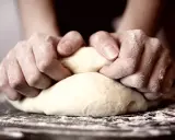 Hände kneten Teig, um die perfekte Konsistenz für Pizza zu erreichen. Die Frage "wie lange pizzateig kneten" beschäftigt viele Hobbybäcker.