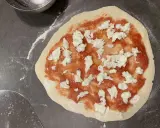 Ein roher Pizzaboden mit Tomatensauce und Mozzarella. Der pizzateig zieht sich zusammen, bereit für den Ofen.