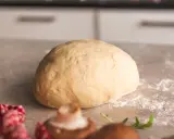 Frischer, goldgelber Pizzateig liegt bereit zum Formen. Ein paar Pilze und Rucola deuten auf eine leckere Pizza hin.