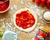 Pizza-Zutaten auf Holzbrett: Teig mit Tomatensauce, Mozzarella, frische Tomaten, Basilikum, Mehl und eine Dose San Marzano Tomaten. Die Frage "wieviel Tomatensauce pro Person" wird hier visuell beantwortet.