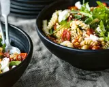 Zwei Schalen mit einem köstlichen nudelsalat mit getrockneten tomaten, Pinienkernen und Rucola.