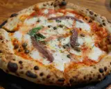 Eine original Pizza mit geschmolzenem Käse, Sardellen, Kapern und Basilikum.