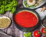 Schüssel mit original italienischer pizzasauce, umgeben von frischem Basilikum, Tomaten, Knoblauch, Salz und Pfeffer.