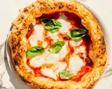 Eine klassische Pizza Napoli mit Tomaten, Mozzarella und frischem Basilikum. Der Belag ist einfach, aber perfekt für diese neapolitanische Spezialität.