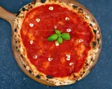 Eine köstliche Pizza Marinara mit Tomatensauce, Knoblauchscheiben und frischem Basilikum auf einem Holzbrett.