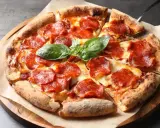 Eine köstliche Pizza mit geschmolzenem Käse und vielen Scheiben italienischer Salami, garniert mit frischem Basilikum.