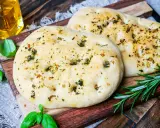 Zwei fluffige Pizzabrote mit Kräutern, perfekt gebacken mit Trockenhefe. Daneben frisches Basilikum und Rosmarin.