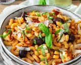 Ein köstlicher mediterraner Nudelsalat mit Pasta, Oliven, Mozzarella-Bällchen und frischem Basilikum, garniert mit Parmesan.