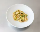Spaghetti alla Nerano, ein cremiges Pastagericht mit gebratenen Zucchinischeiben, garniert mit frischen Kräutern, serviert auf einem weißen Teller.