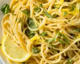 Spaghetti al limone, garniert mit frischem Basilikum und Zitronenschale, serviert mit einer Zitronenspalte.