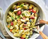 Ein cremiger Tortellini Salat mit Kirschtomaten, Oliven und Kräutern, serviert in einer Schüssel mit Holzspateln.