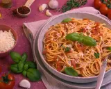 Ein Teller Spaghetti Napoli mit Tomatensauce, Basilikum und Parmesan. Daneben frische Tomaten, Knoblauch und Kräuter.