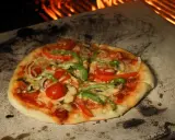 Eine köstliche Pizza mit Tomaten, Paprika und Pilzen wird auf einem Pizzastein im Ofen gebacken, wo die Flammen lodern.