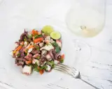 Frischer Insalata di polpo mit Tomaten, Petersilie und Limettenspalten auf einem Teller, daneben ein Glas Weißwein.