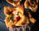 Hand hält einen herzhaften Pizza-Muffin mit geschmolzenem Käse, Wurst und grünen Paprika.