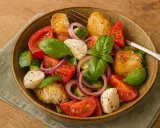 Ein köstlicher italienischer Salat mit Tomaten, Mozzarella, Gurken, roten Zwiebeln und Croutons, garniert mit frischem Basilikum.