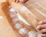 Hände rollen Teig auf Backpapier aus. Perfekt, um gegangenen Pizzateig einzufrieren und später zu verwenden.