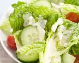 Frischer Romana Salat mit Gurkenscheiben und Tomaten, beträufelt mit cremigem Dressing.
