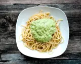 Spaghetti mit cremigem Avocado Pesto auf einem weißen Teller, serviert auf rustikalem Holz.
