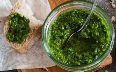 Frisches schnittlauch pesto in einem Glas, mit einem Löffel darin. Ein Stück Brot mit dem grünen Pesto darauf liegt daneben.