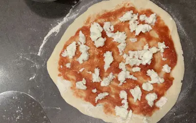 Ein roher Pizzaboden mit Tomatensauce und Mozzarella. Der pizzateig zieht sich zusammen, bereit für den Ofen.