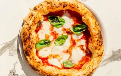 Eine klassische Pizza Napoli mit Tomaten, Mozzarella und frischem Basilikum. Der Belag ist einfach, aber perfekt für diese neapolitanische Spezialität.