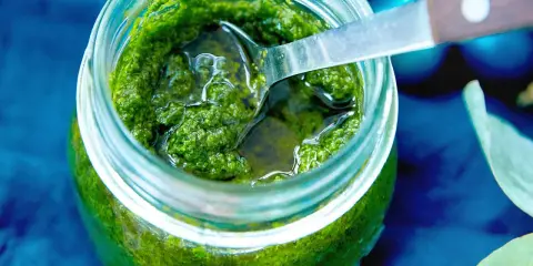 Frisches Rucola Pesto in einem Glas, bereit zum Genießen. Eine Löffelspitze ragt heraus.