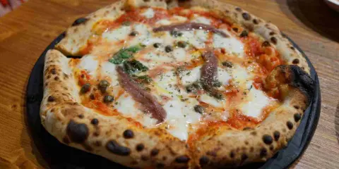 Eine original Pizza mit geschmolzenem Käse, Sardellen, Kapern und Basilikum.