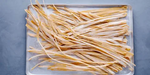 Frische, selbstgemachte Tagliatelle liegen auf einem Blech, bereit zum Kochen. Das Ergebnis von Tagliatelle selber machen.