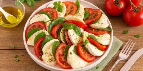 Ein köstlicher Tomate Mozzarella Salat, kunstvoll arrangiert mit frischem Basilikum und beträufelt mit Olivenöl.