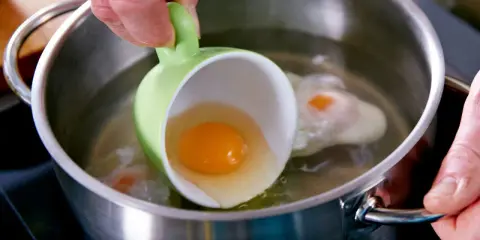 Ein rohes Ei wird aus einer grünen Tasse in kochendes Wasser gegossen, um Eier zu pochieren.