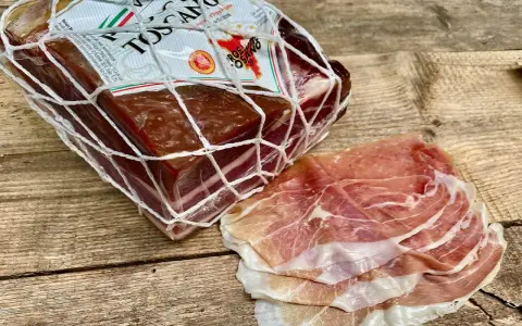 Ein Block **Prosciutto Toscano** im Netz und daneben dünn geschnittene Scheiben.