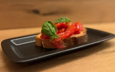 Eine Scheibe geröstetes Brot mit frischen Tomaten und Basilikum, die Haupt-Bruschetta-Zutaten, auf einem schwarzen Teller.