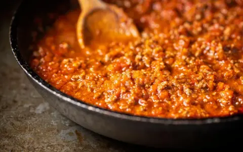 Eine Pfanne mit köstlicher, original italienischer Bolognese-Sauce, die mit einem Holzlöffel umgerührt wird.