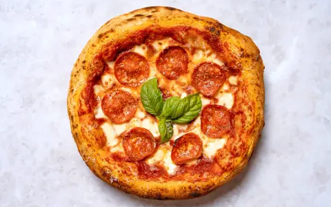 Eine köstliche New York Style Pizza mit Salami und frischem Basilikum, bereit zum Genießen.