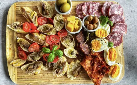 Ein köstlicher Antipasti-Abend mit Bruschetta, Sardellen, Tomaten, Oliven, Käse, Eiern und Salami auf einem Holzbrett.